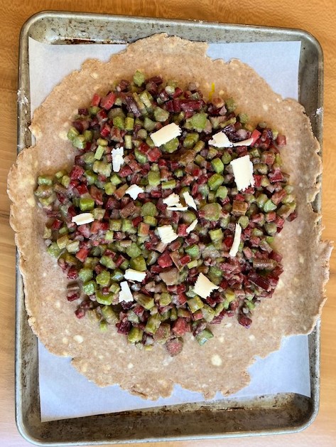 Pie crust rolled out with rhubarb filling and butter dotted on top