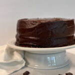 Chocolate Cake Freshly Milled Flour on a white cake stand with bits of chocolate on the countertop