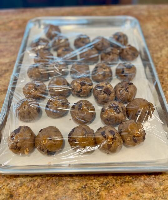 freshly milled chocolate chip cookies on a tray covered with plastic wrap