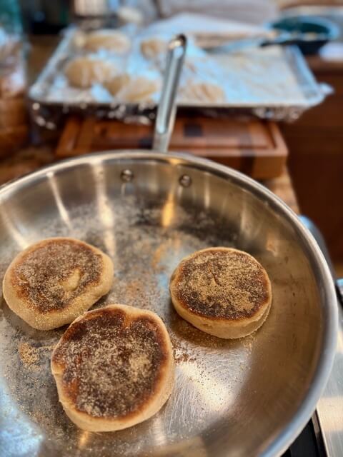 three fresh milled english muffins in a pan cooking