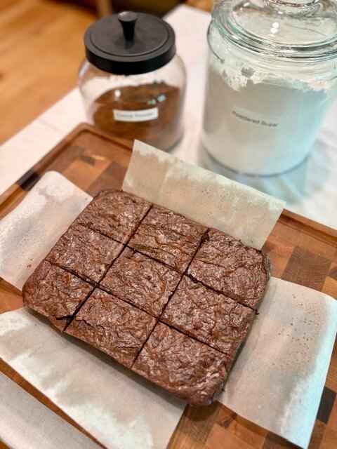 Fresh Milled Flour Brownies on a cutting board with cocoa powder and sugar behind them