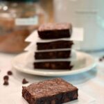 Fresh Milled Flour Brownie with a stack of brownies behind it and some chocolate chips on the countertop