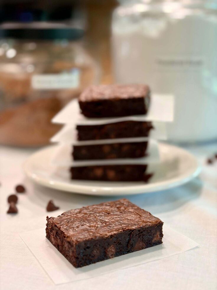 Fresh Milled Flour Brownie with a stack of brownies behind it and some chocolate chips on the countertop