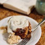 Fresh Milled Cinnamon Roll on a white plate next to a book and cup of coffee