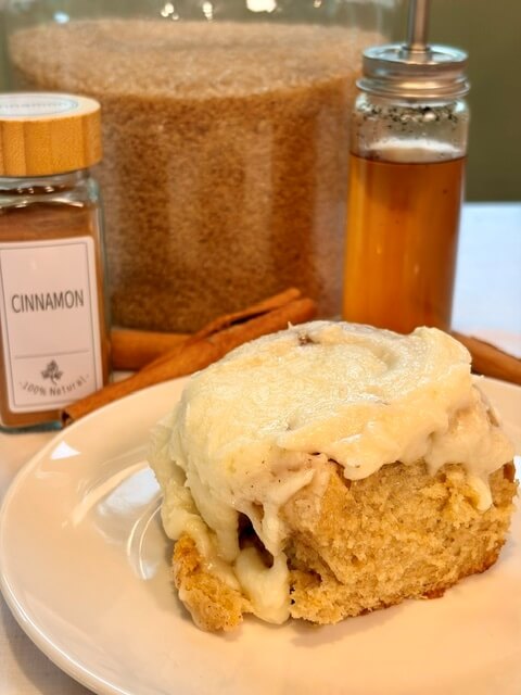 Sourdough Cinnamon Roll on a white plate with cinnamon and brow sugar and vanilla behind it