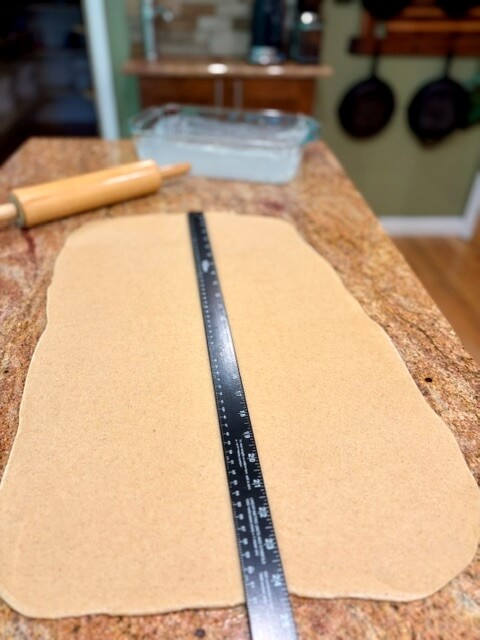 Dough rolled out on counter with a yardstick on top to show the length and rolling pin and pan in the background