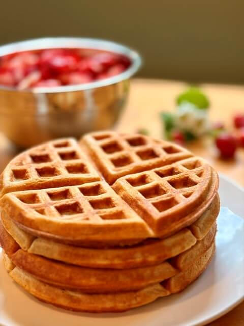 A stack of fresh milled flour waffles with strawberries in the background