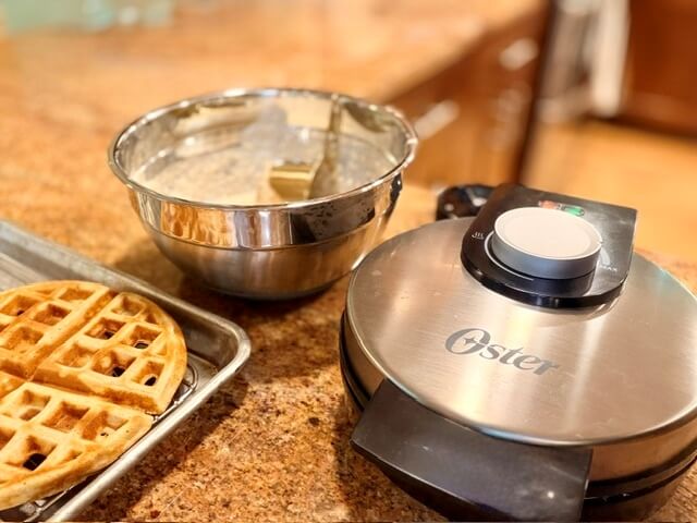 Waffle maker, bowl of batter and waffles on a wire rack