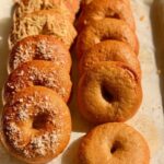 A dozen fresh milled flour bagels sitting in two rows on a cookie sheet