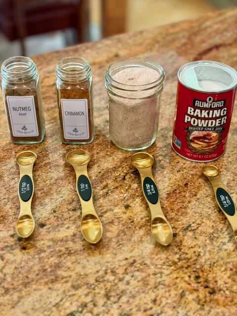 cinnamon, nutmeg, salt and baking powder on a counter with measuring spoons in front of them
