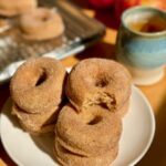 fresh milled flour apple cider doughnuts on a white plate and apples in the background