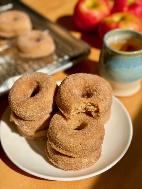 fresh milled flour apple cider doughnuts on a white plate and apples in the background